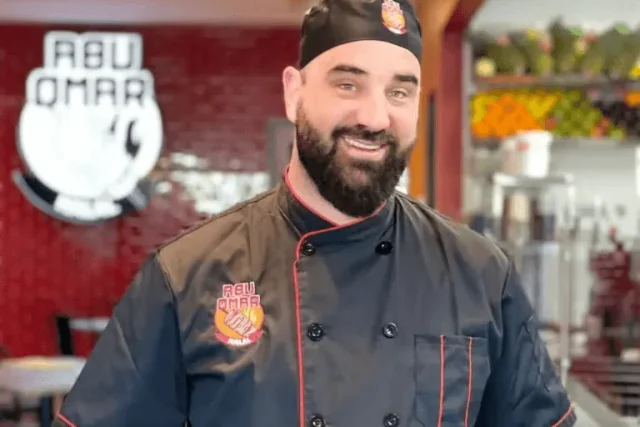 Mohammad Altawaha, known as Abu Omar, in an Abu Omar Halal chef's jacket in front of the restaurant's wall logo