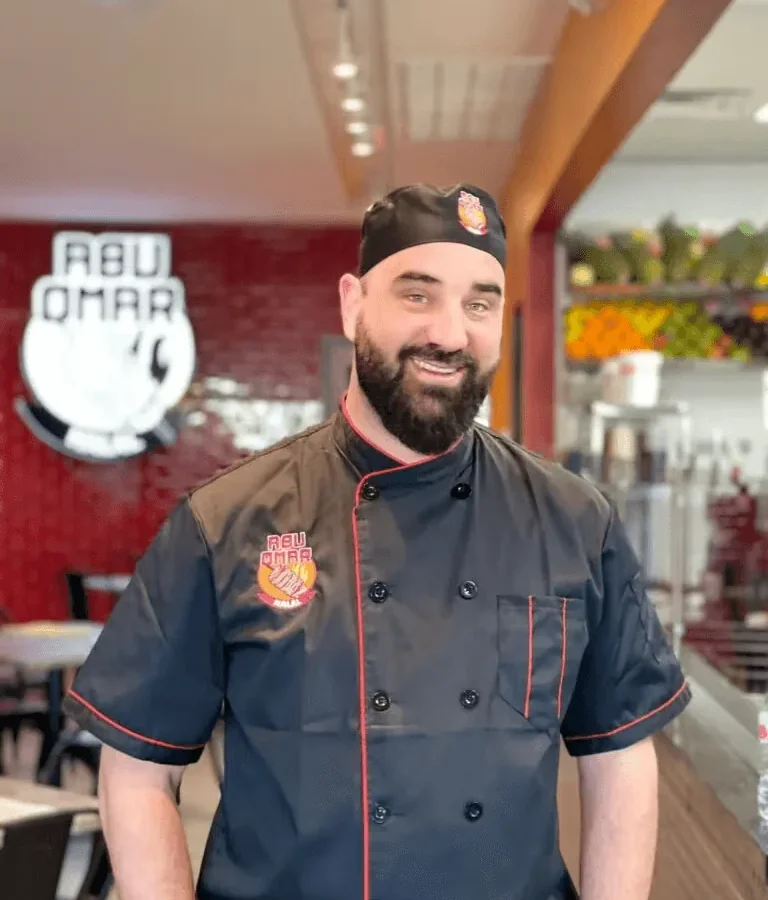 Mohammad Altawaha, known as Abu Omar, in an Abu Omar Halal chef's jacket in front of the restaurant's wall logo