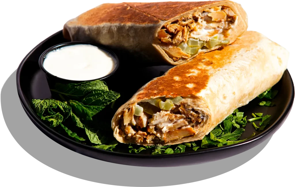 A chicken shawarma wrap cut in half on a black plate, served with garlic sauce and chopped parsley