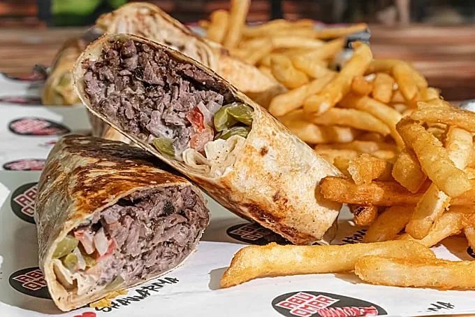A beef shawarma wrap cut in half and served with seasoned fries on Abu Omar Halal branded paper