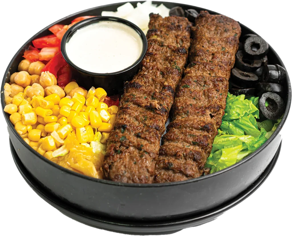 Two grilled beef kofta skewers over a salad of lettuce, tomatoes, corn, chickpeas and olives