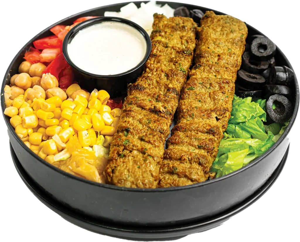 Two grilled chicken kofta skewers over a salad of lettuce, tomatoes, corn, chickpeas and olives